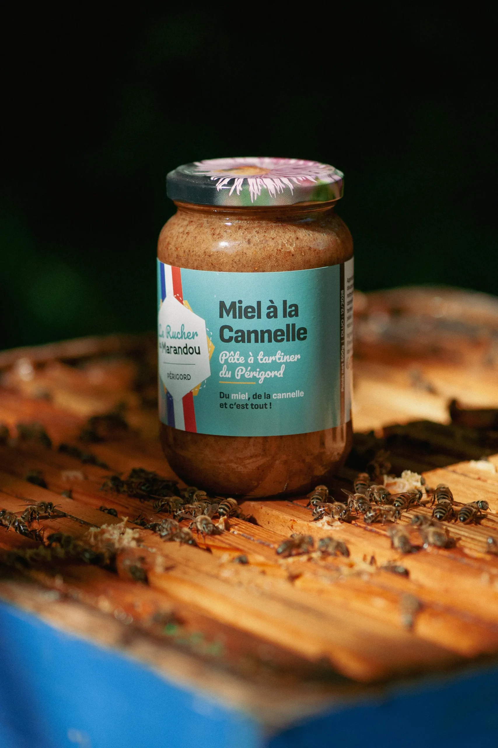 Pot de miel à la cannelle du Périgord de notre production posé sur une ruche avec des abeilles – Rucher du Marandou