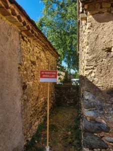 Panneau "Attention abeilles" installé entre deux maisons en pierre du Périgord à proximité d'une colonie d'abeilles installée dans un mur.