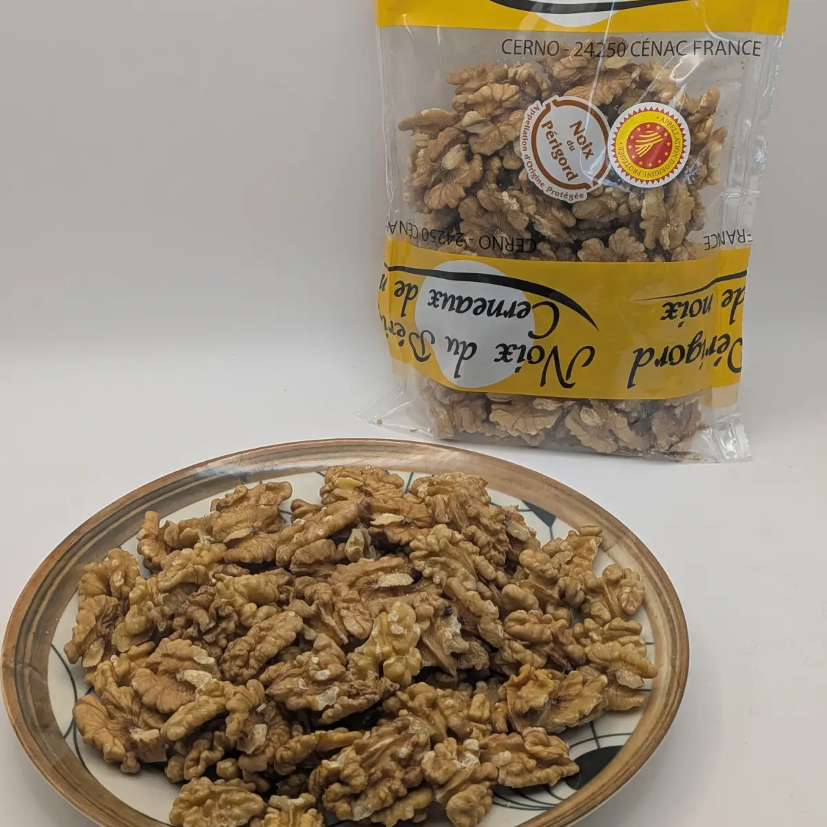 Demi-cerneaux de noix du Périgord AOP Extra Moitié présentés dans une assiette, avec leur sachet en arrière-plan